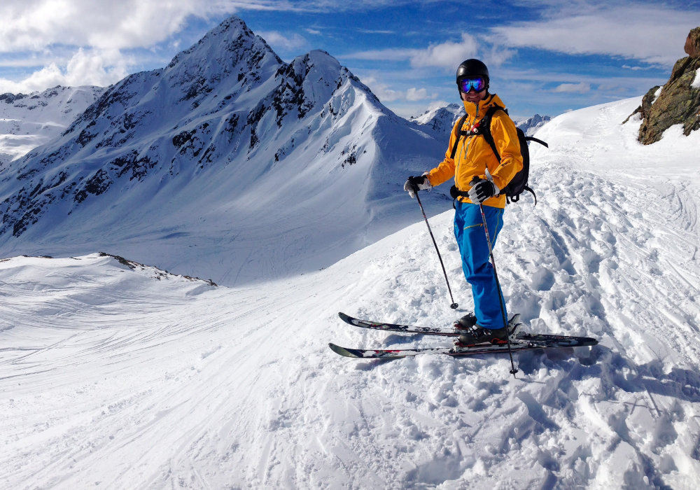 Man in Ski Outdoor Wear poses at the top of a snowy mountain