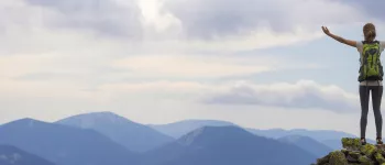 Woman hiker with backpack stand on top of a hill overlooking mountains