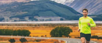 Man in sportswear running on a road with mountains in the background