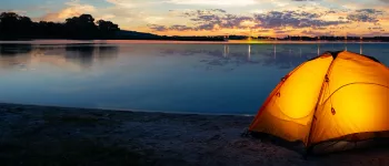 orange tent with light on inside at the side of a lake at dusk